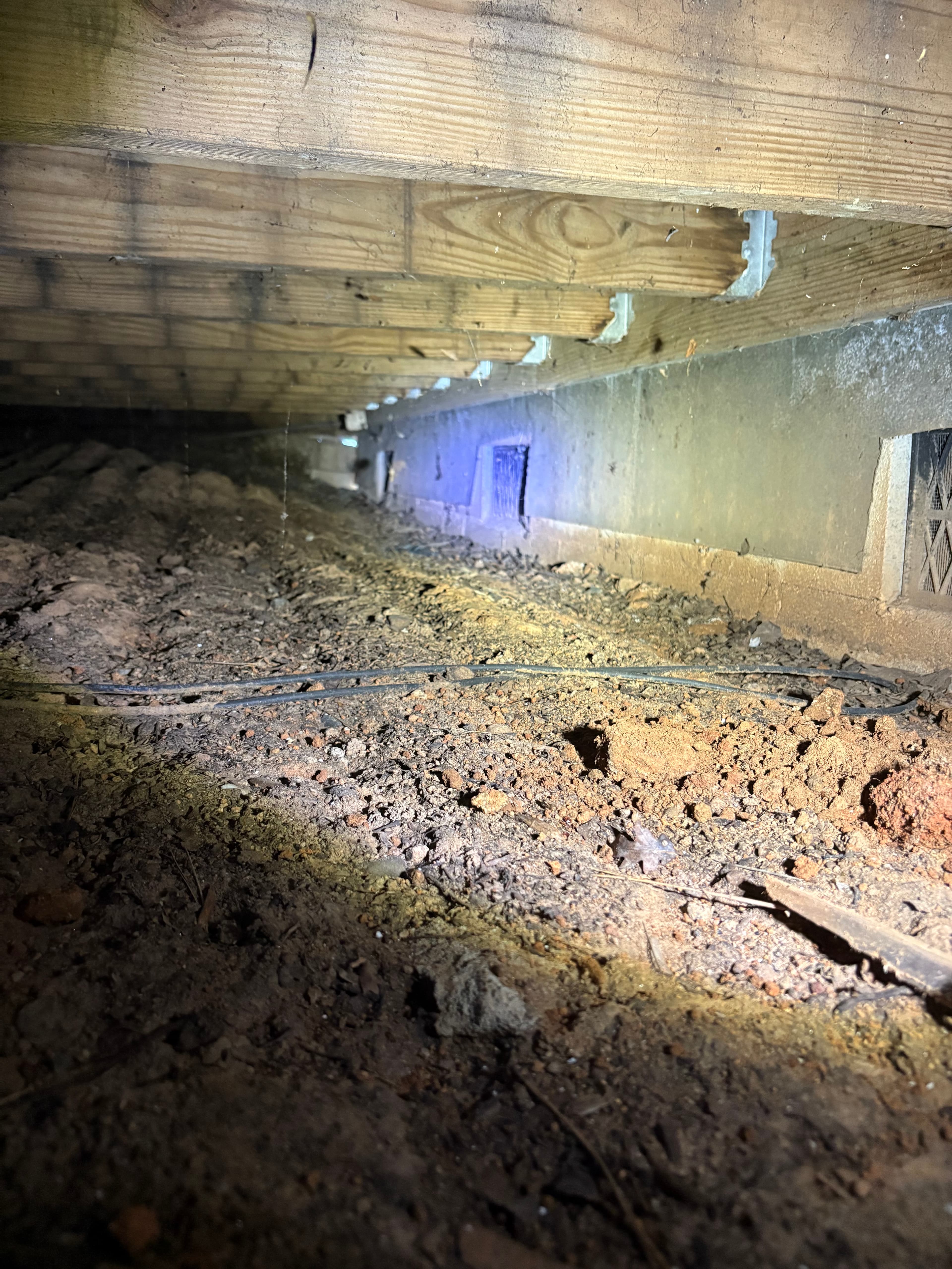 A bare-dirt crawl space along the foundation wall with no drainage in place