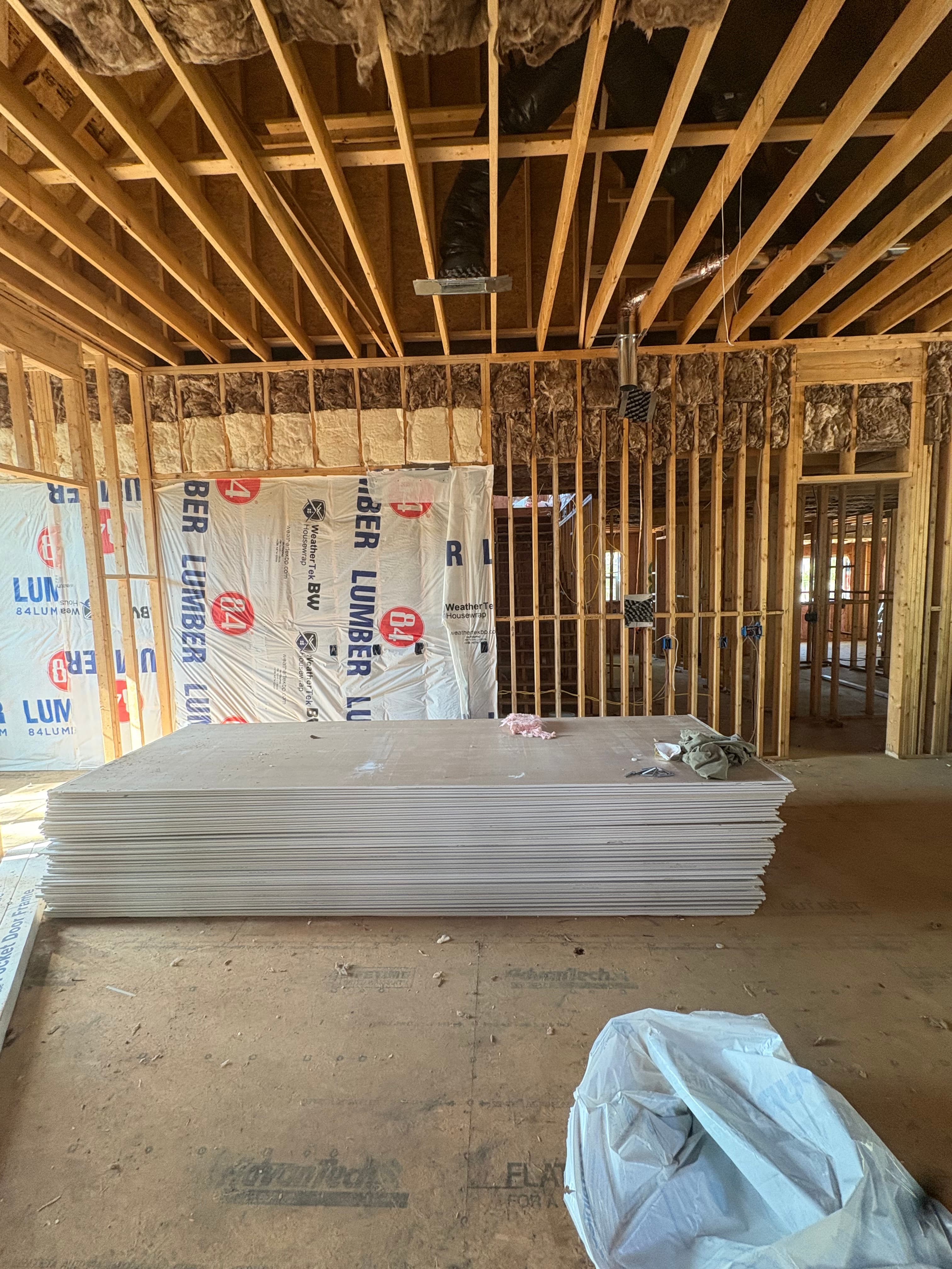 Batt insulation installed in a framed corner with house wrap visible and drywall staged nearby