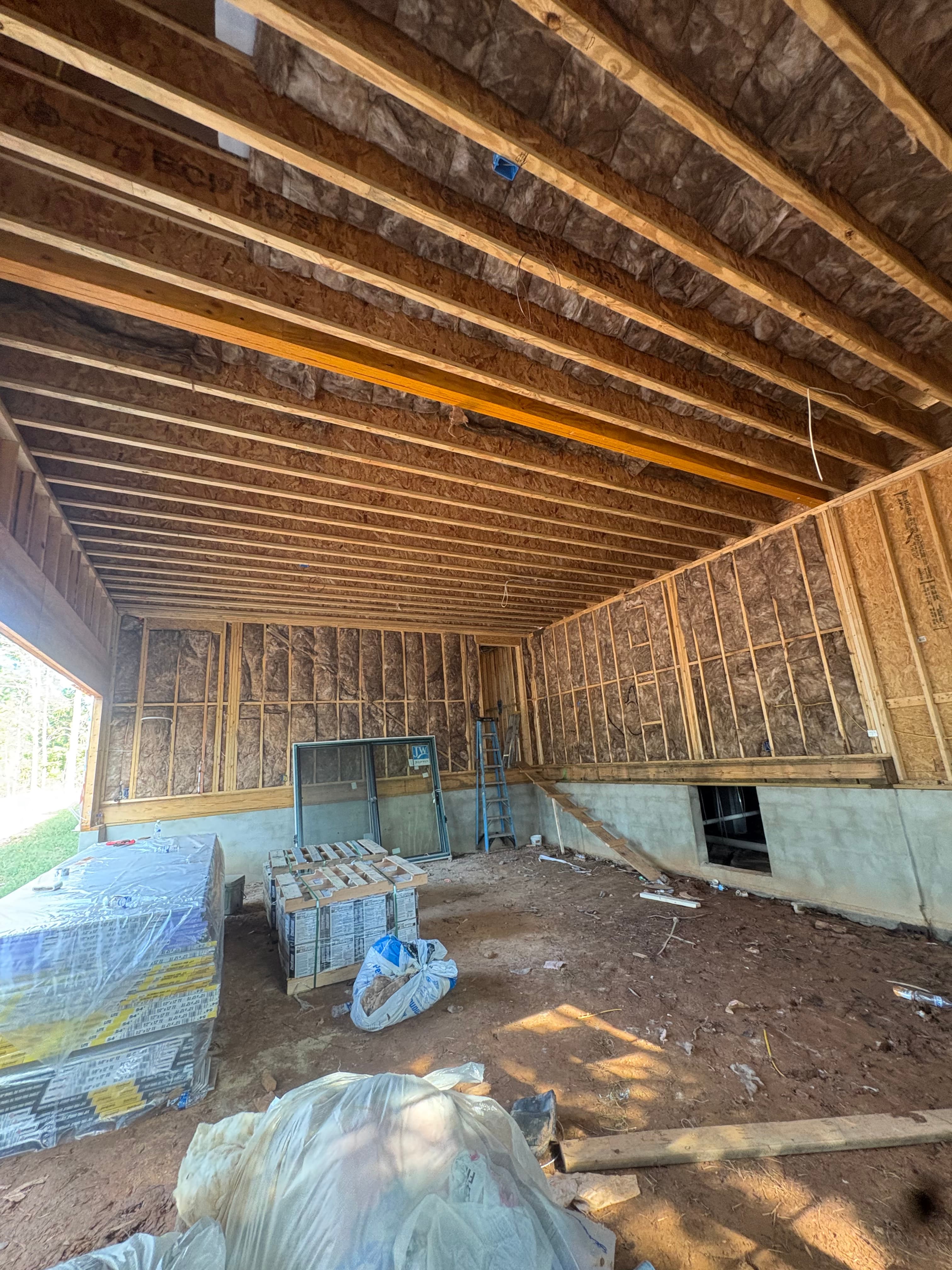 Batt insulation installed in roof rafters on a new-construction home, with insulation staged outside