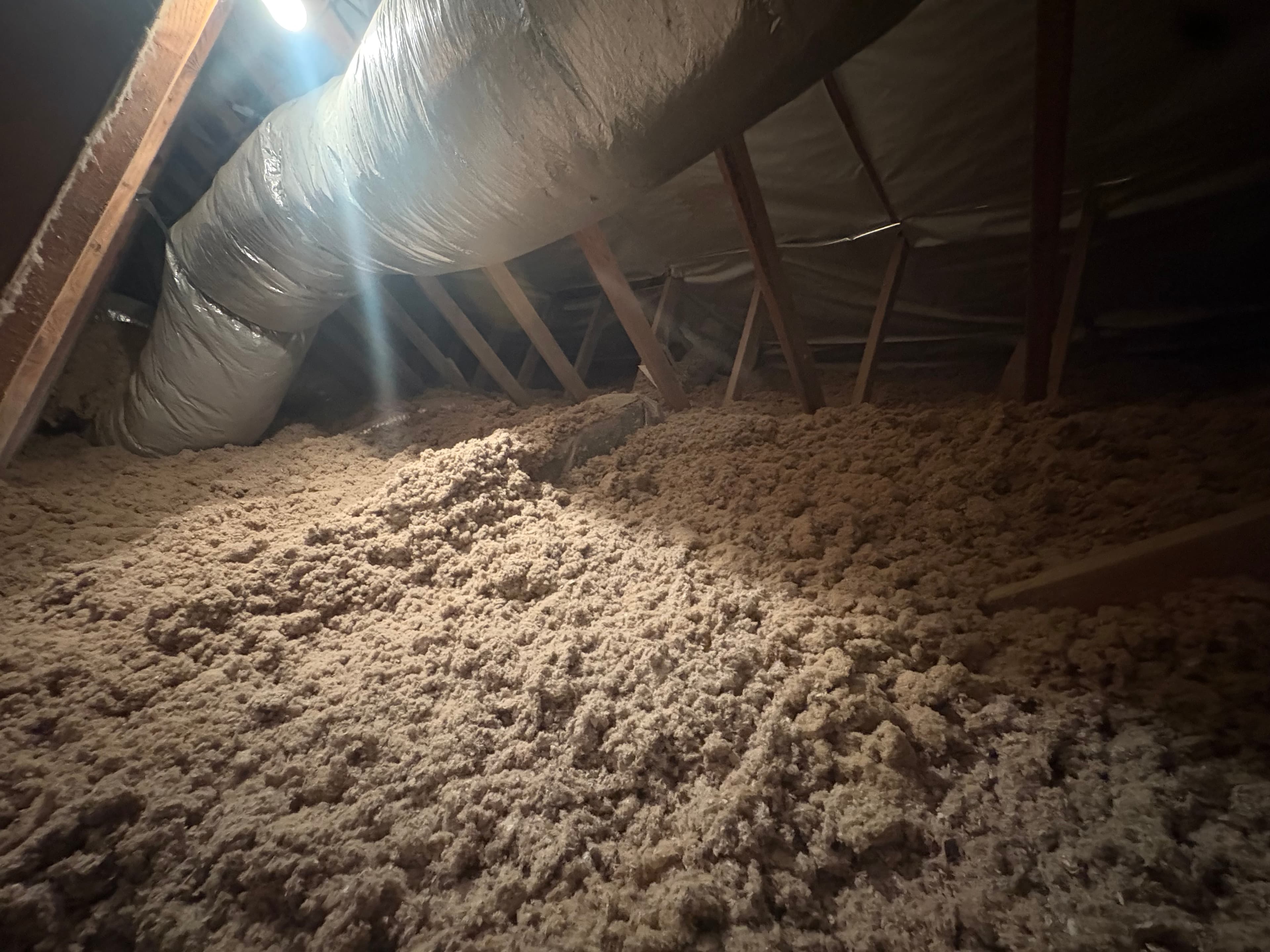 Blown-in insulation filling an attic floor around ductwork and framing
