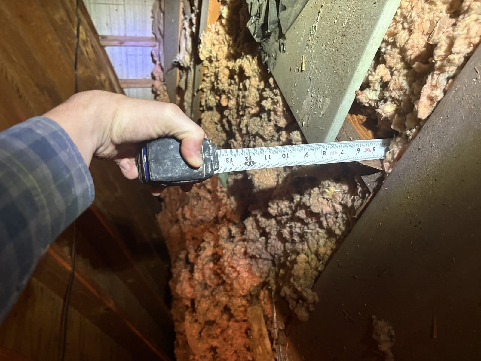 Measuring existing insulation depth with a tape measure during a free attic inspection