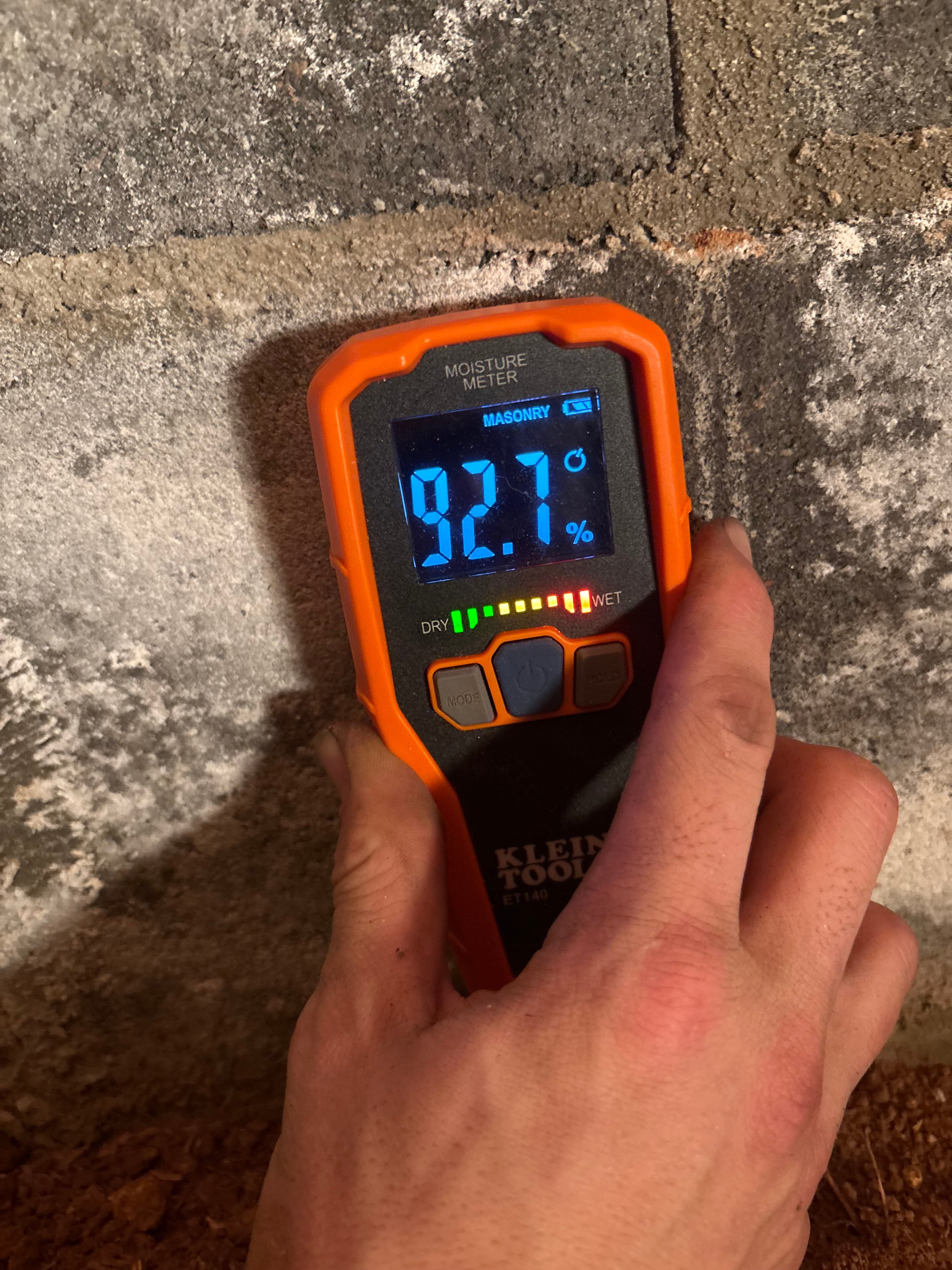 A moisture meter reading high humidity on a crawl space foundation wall